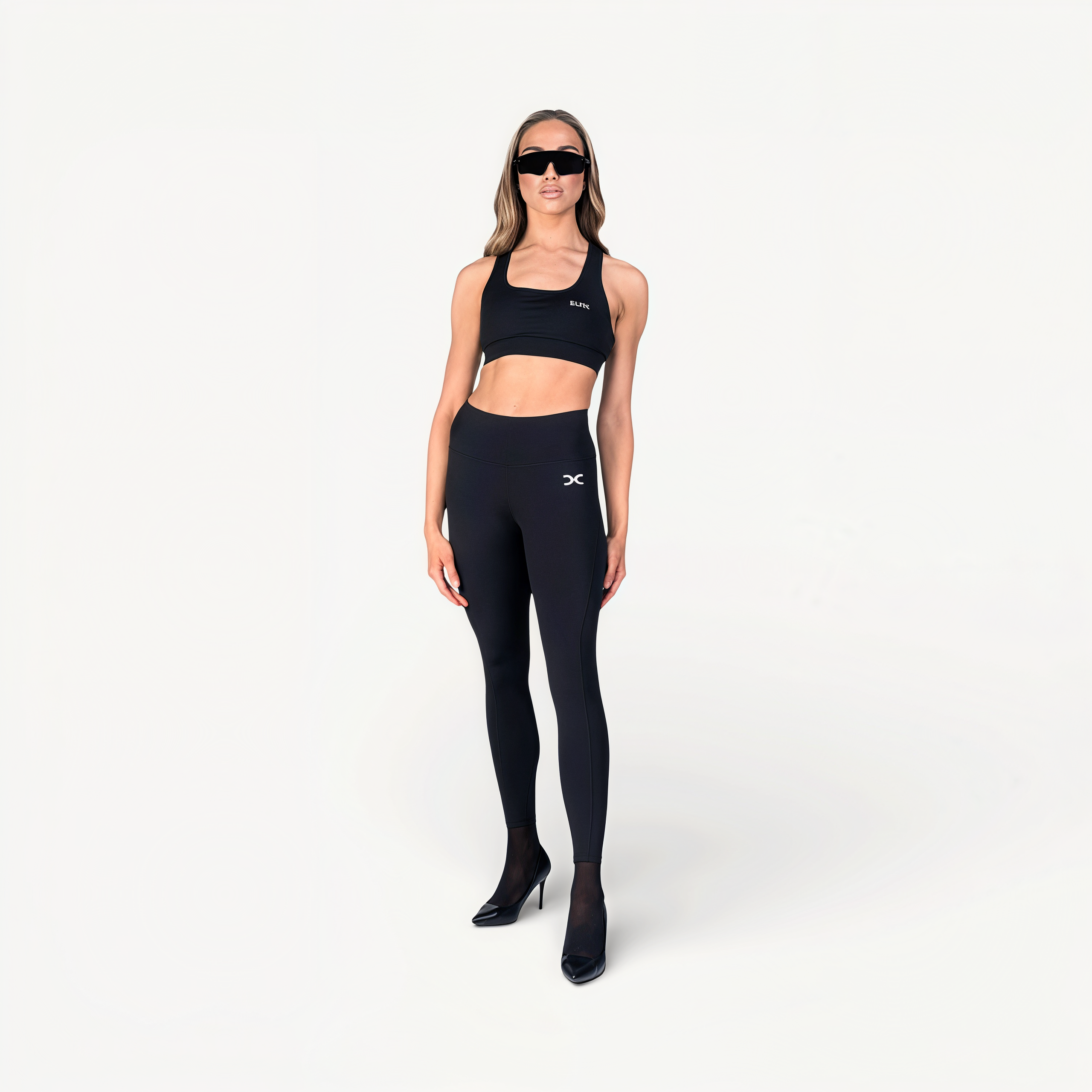 Woman wearing black athletic leggings and sports bra with ‘Elite’ ENVOLE on a white background front view.