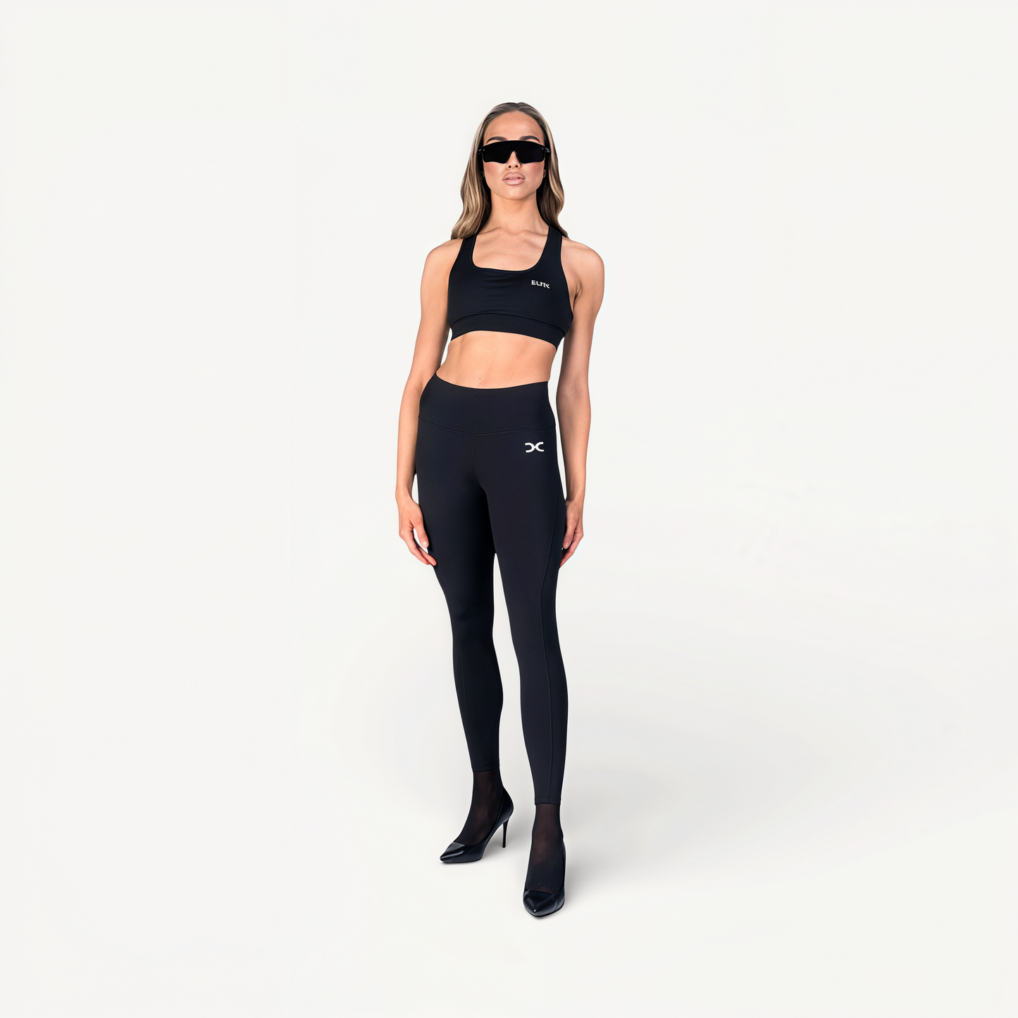 Woman wearing black athletic leggings and sports bra with ‘Elite’ ENVOLE on a white background front view.