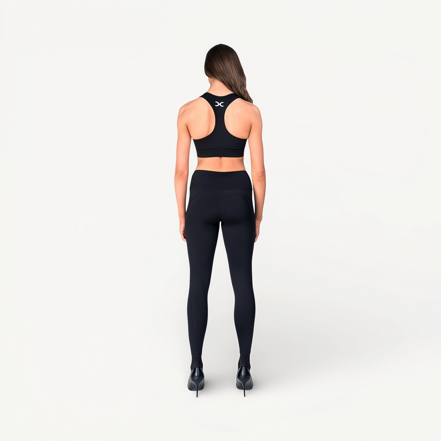 Woman wearing black athletic leggings and sports bra with ‘Elite’ ENVOLE on a white background back view.